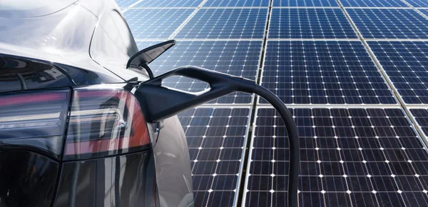 Close up of electric car with a connected charging cable on the background of solar panels. High quality photo
