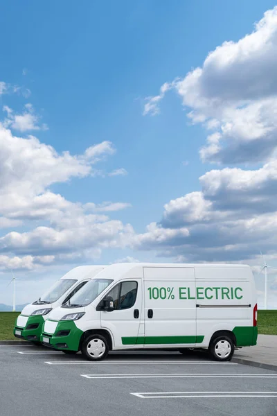 Electric vans parked in a row. Wind turbines in a horizon. High quality photo