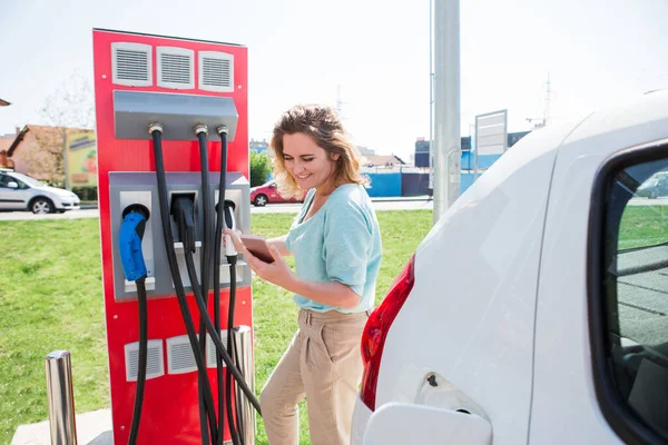 一名妇女站在充电站 并持有一辆电动车的充电器插头 — 图库照片