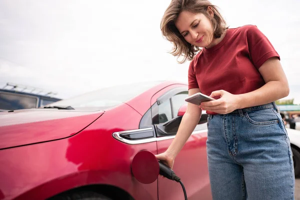 Vrouw Met Smartphone Opladen Rode Elektrische Auto — Stockfoto