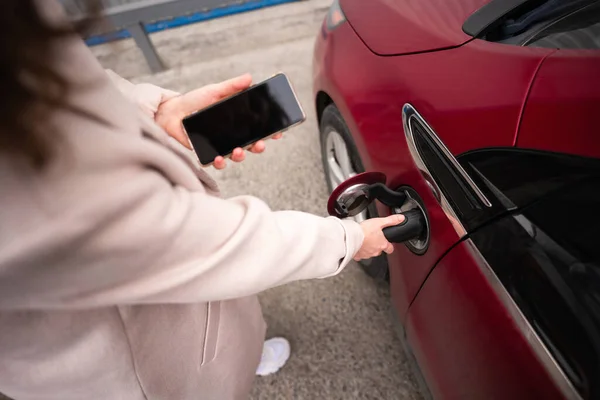 拿着智能手机给红色电动车充电的女人 — 图库照片