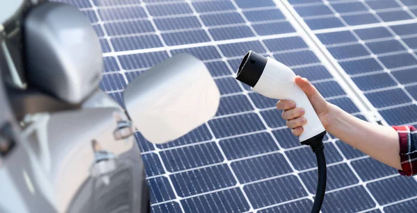 ソーラーパネルを背景に電気自動車充電プラグと手 — ストック写真