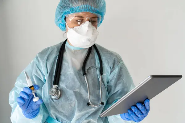 Doctor stands with tablet computer and a syringe.
