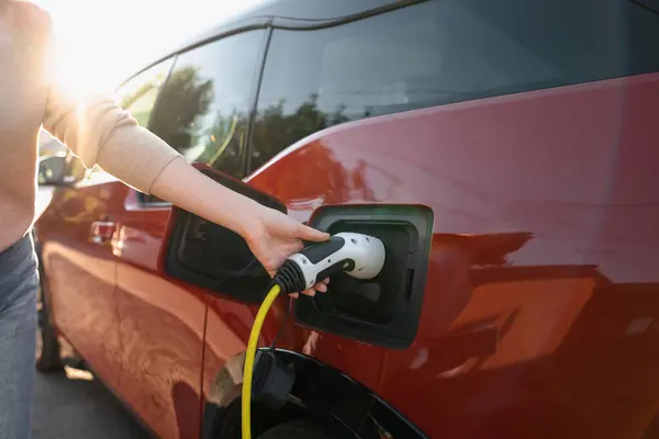 Woman holds plug of electric car charging station..