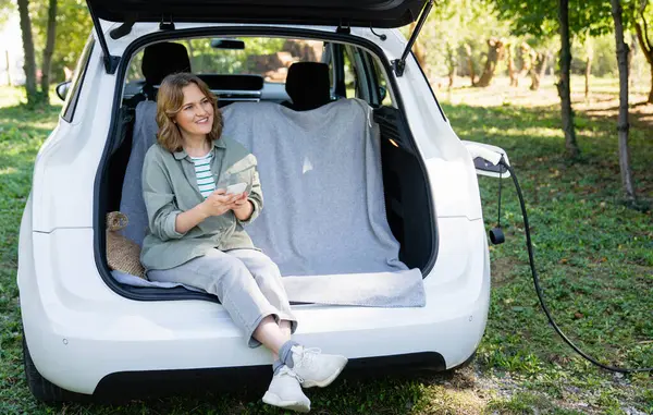 Woman Smartphone Sits Electric Car Trunk — Stock Photo, Image