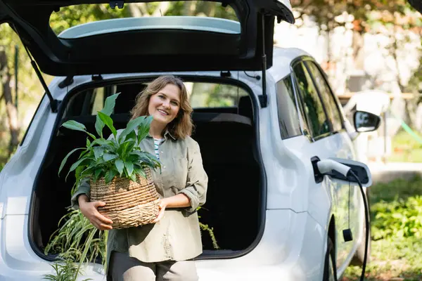 Vrouw Met Plant Pot Naast Een Oplaadbare Elektrische Auto Tuin — Stockfoto