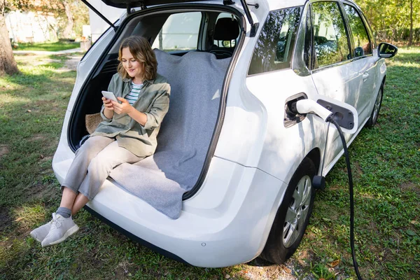Donna Con Smartphone Siede Nel Bagagliaio Auto Elettrica — Foto Stock