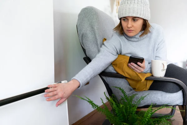 Woman Warm Clothes Smartphone Sits Close Heating Radiator Low Temperature — Stock Photo, Image