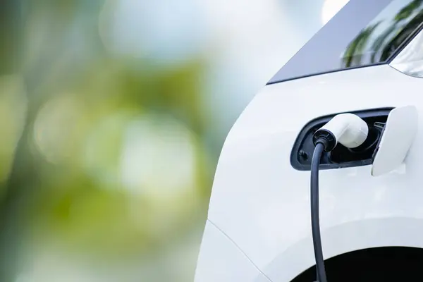 Close up of electric car inlet with a connected charging cable on a green background.