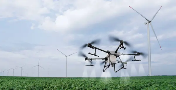 Drone sprayer flies over the agricultural field. Wind turbines on a horizon..Drone sprayer flies over the agricultural field. Wind turbines on a horizon