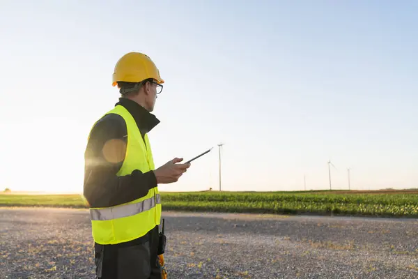 stock image Engineer with digital tablet works on a field of wind turbines.