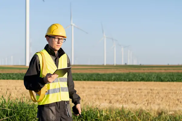 stock image Engineer with digital tablet works on a field of wind turbines.