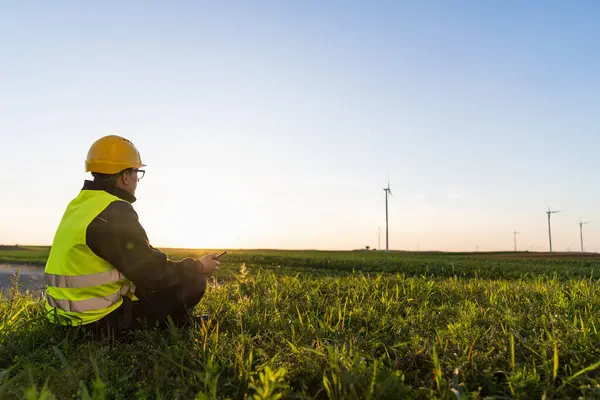 stock image Worker sits on the grass and looks at wind turbines.