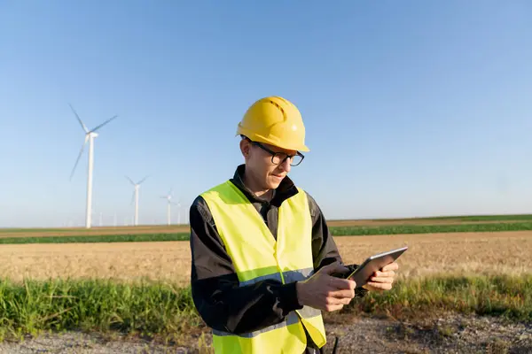 stock image Engineer with digital tablet works on a field of wind turbines.