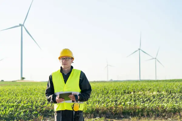 stock image Engineer with digital tablet works on a field of wind turbines.