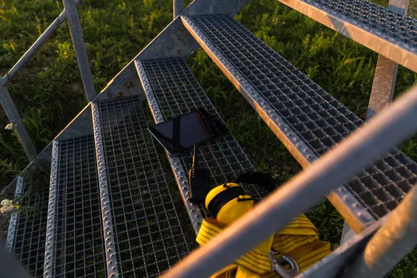 stock image Digital tablet, headphones and climber's rope are on the ladder of the wind turbine.