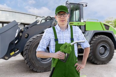 Man with biofuel nozzle on a background of construction machines.. clipart