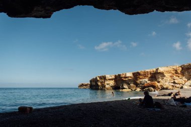 Büyük kayalar çakıl taşı plajında suya batar..
