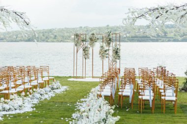 Nehir kıyısında, salkımlı ağaçlı yeni evliler için düğün töreni için özel kemer. Boş sandalyeler ve şemsiyeler