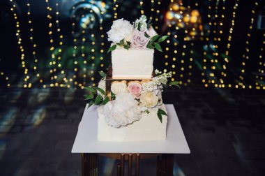 Üç katlı büyük kare düğün pastası. Kurşunlu ışığın arka planına karşı. Ukrayna 'da birinci sınıf düğün. Akşam lambalarının altında düğün tatlısı. Düğün dekoru.