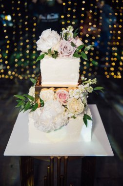 Üç katlı büyük kare düğün pastası. Kurşunlu ışığın arka planına karşı. Ukrayna 'da birinci sınıf düğün. Akşam lambalarının altında düğün tatlısı. Düğün dekoru.