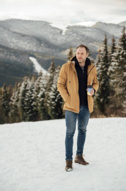 Morning coffee in the mountains. Handsome man drinking coffee and looking at the mountains in Ukraine. Snowy mountain background.