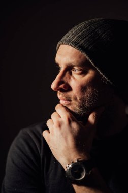 Siyahi stüdyonun arka planında dikilirken ciddi bir dramatik adam başka tarafa bakıyor..