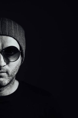 Güneş gözlüklü ciddi bir dramatik adam siyah stüdyonun arka planında dikilirken başka tarafa bakıyor..