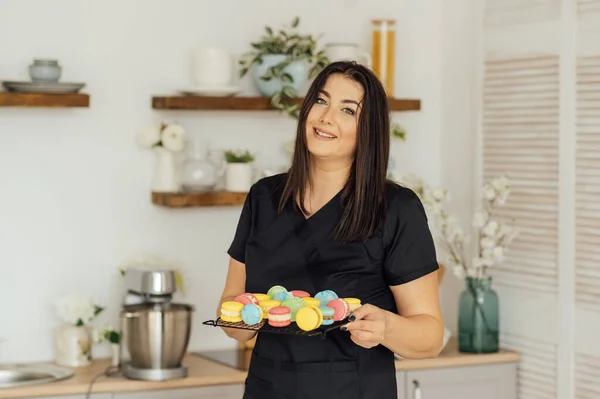 Woman confectioner holding traditional french colorful macarons in a rows on a metal mesh.
