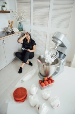 Kadın aşçı blenderin arka planında yerde oturuyor. Bir sürü siparişten yoruldum.