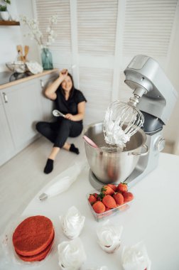 Kadın aşçı blenderin arka planında yerde oturuyor. Bir sürü siparişten yoruldum.