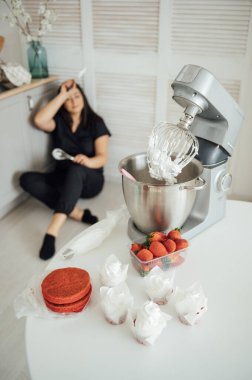 Kadın aşçı blenderin arka planında yerde oturuyor. Bir sürü siparişten yoruldum.