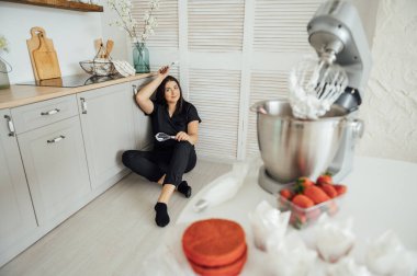 Kadın aşçı blenderin arka planında yerde oturuyor. Bir sürü siparişten yoruldum.