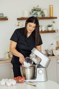 Aşçı kız pastaları süslemek için kremayı mikserden kalıba koyuyor..