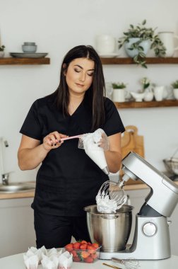 Aşçı kız pastaları süslemek için kremayı mikserden kalıba koyuyor..