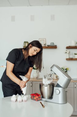 Aşçı kız pastaları süslemek için kremayı mikserden kalıba koyuyor..