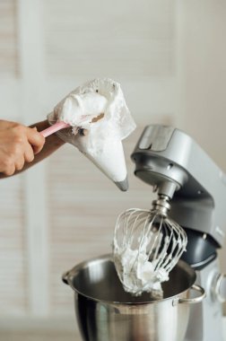 Aşçı kız pastaları süslemek için kremayı mikserden kalıba koyuyor..
