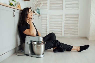 Bir kadın aşçı yerde oturuyor ve yanında profesyonel bir mikser tutuyor. Profesyoneller için yüksek kalite karıştırıcı