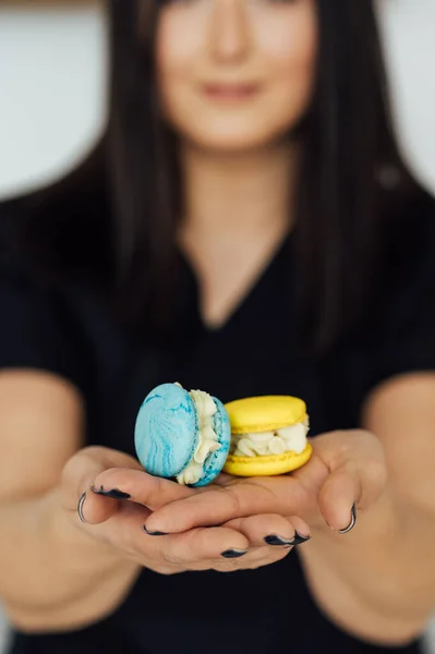 The confectioner is holding two yellow and blue French macarons in her hand. Ukrainian flag colors.