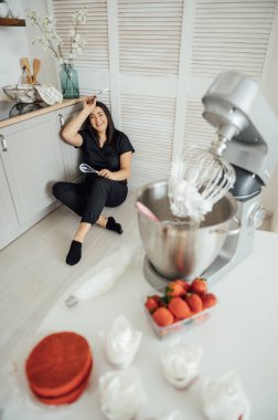 Kadın aşçı blenderin arka planında yerde oturuyor. Bir sürü siparişten yoruldum.
