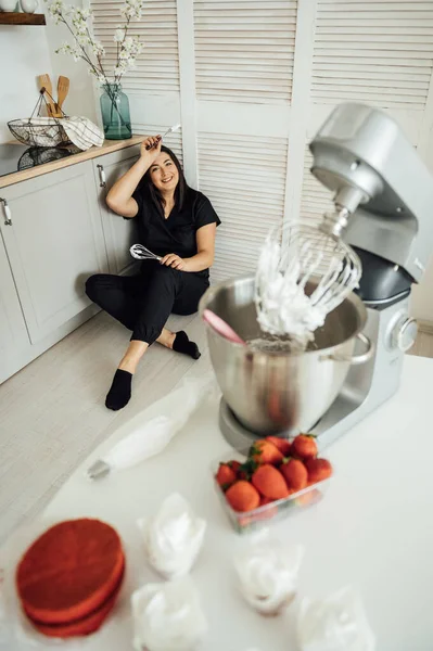 Kadın aşçı blenderin arka planında yerde oturuyor. Bir sürü siparişten yoruldum.