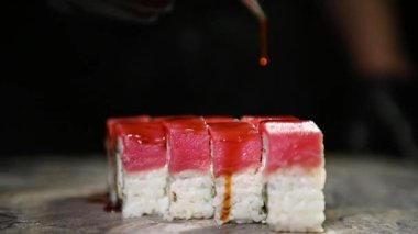 Suşi ustası Philadelphia dürümünün üzerine unagi sosu döküyor. Somon, pirinç, avokado ve peynirli suşi. Geleneksel Japon yemeklerini deniz ürünleri ve balıklarla pişirmek. Suşi takımını kapat..