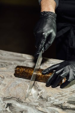 Suşi rulosu, nori 'ye sarılmış, siyah eldivenli şef bıçakla kesiyor. Suşi çiğ balıktan yapılır..