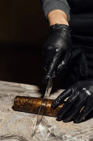 stock image Sushi roll, wrapped in nori, the chef in black gloves cuts with a knife. Sushi is made from raw fish.