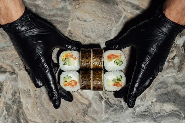 寿司卷 包裹在诺里 厨师戴着黑色手套 用刀切割 寿司是生鱼片做的 — 图库照片