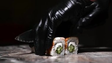 Philadelphia usulü suşi pişirme işlemi yakın çekim. Suşi ustası ruloyu keskin bir bıçakla parçalara ayırıyor. Geleneksel Japon yemekleri ve deniz ürünleri..