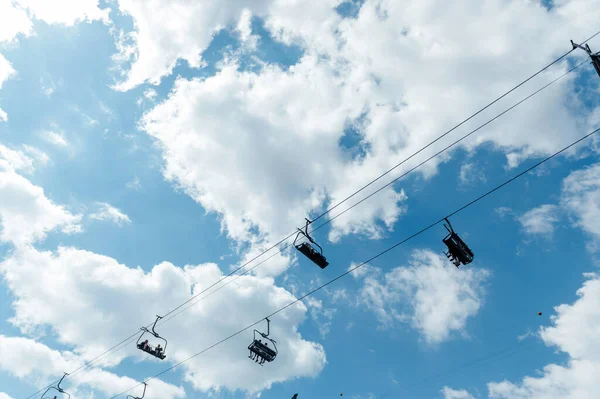 山の4つの青い雲の空の背景にシーターチェアリフト 観光客は風景を見て移動します — ストック写真