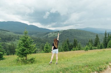 Saç stili olan güzel bir kadın. Bir sürü örgülü. Siyah tişört ve şortla dağın tepesinde poz veriyor.