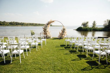 Nehir kenarında bir düğün merasimi için yuvarlak kemer. Beyaz cam sandalyeler misafirler için. Yakın çekim, kopyalama alanı, ayarlı. Davetiye, aşk konsepti