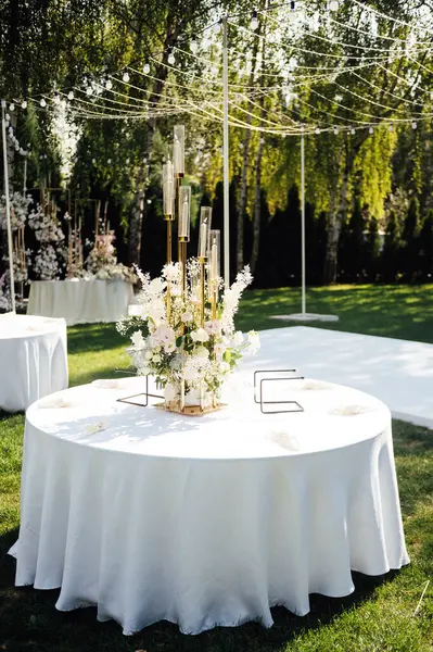 Wedding. Banquet. The chairs and round table for guests, served with cutlery, greenery flowers and crockery and covered with a white tablecloth. olive color